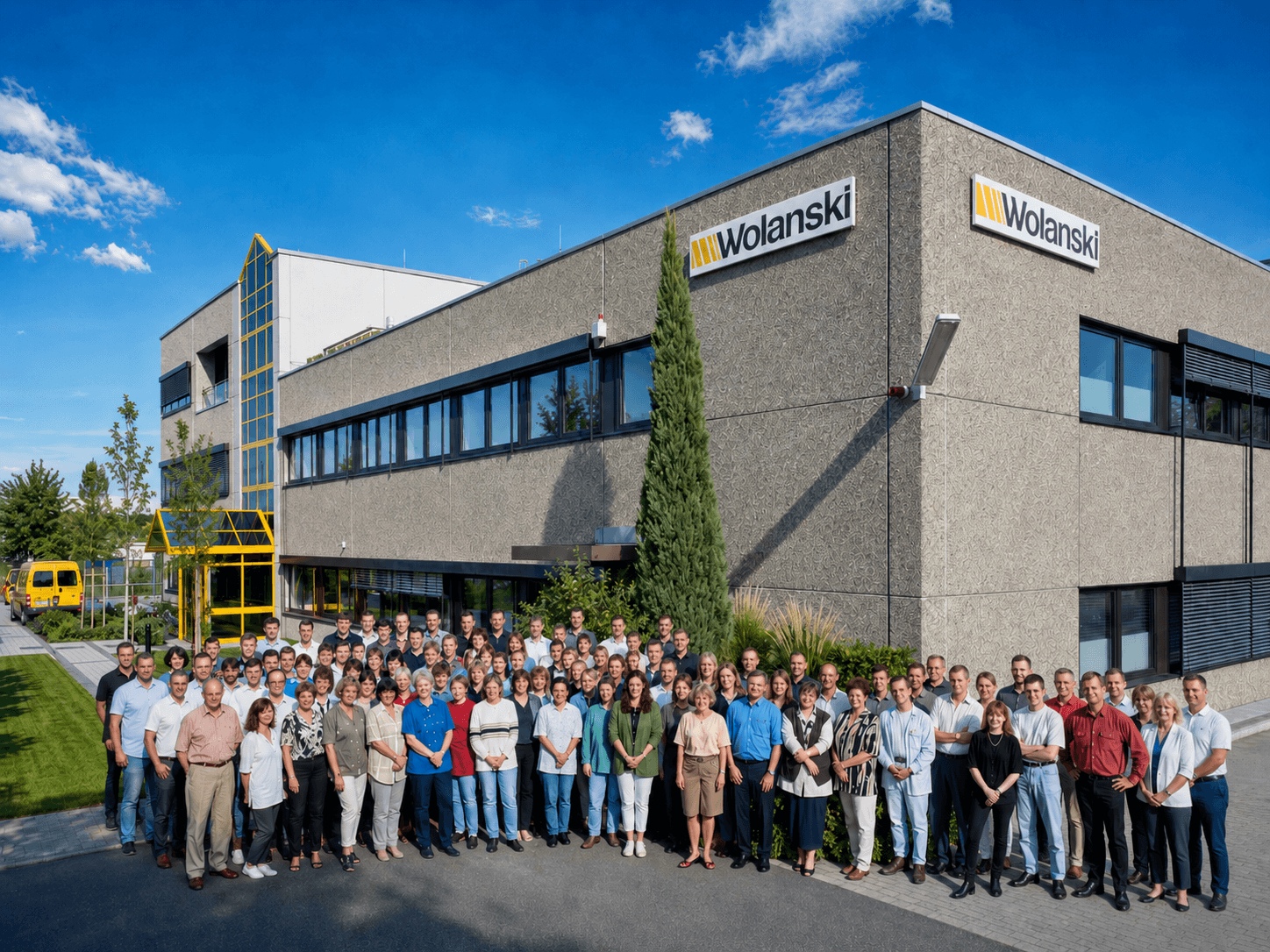 Gruppenfoto der Mitarbeitenden der Wolanski GmbH vor dem Firmengebäude. An der Fassade sind zwei Wolanski Logos zu sehen.